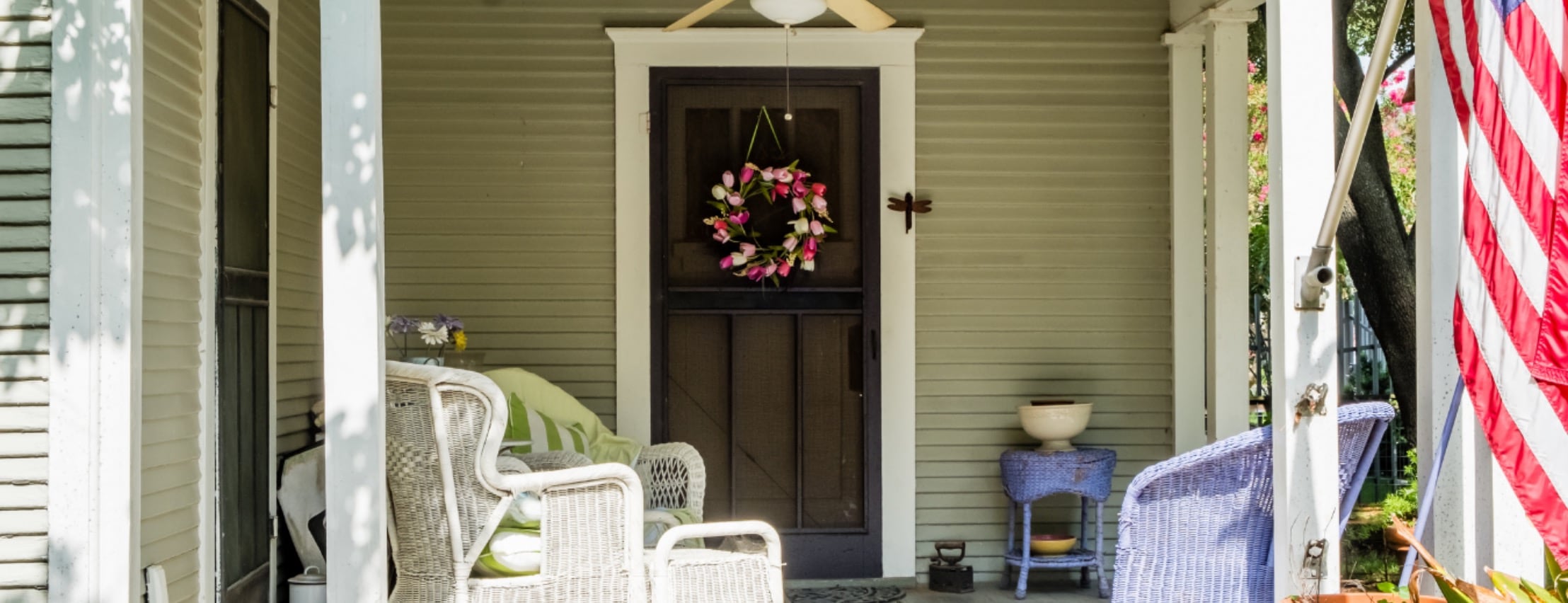 A southern front porch decorated with white wicker furniture an american flag and a wreath on the door