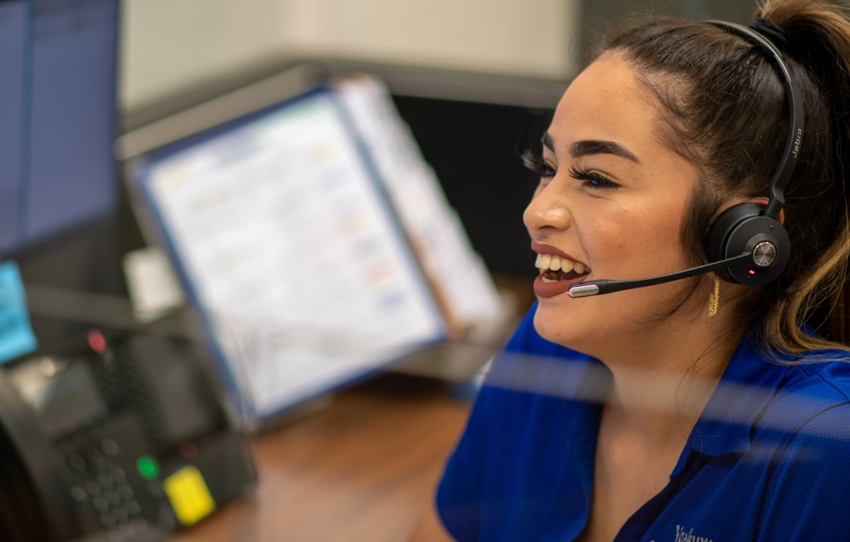 A female customer service representative wears a headset and smiles while looking forward